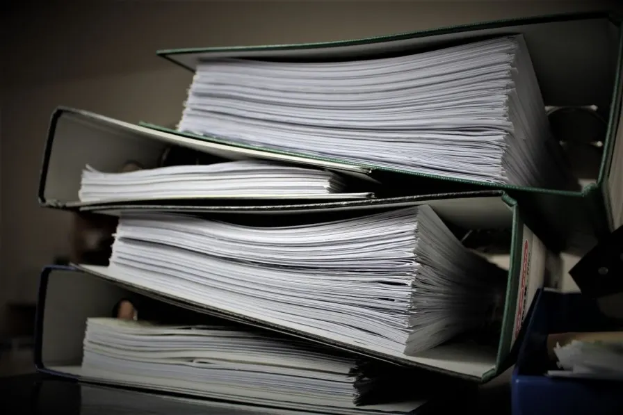 Binders overflowing with stacks of paper records
